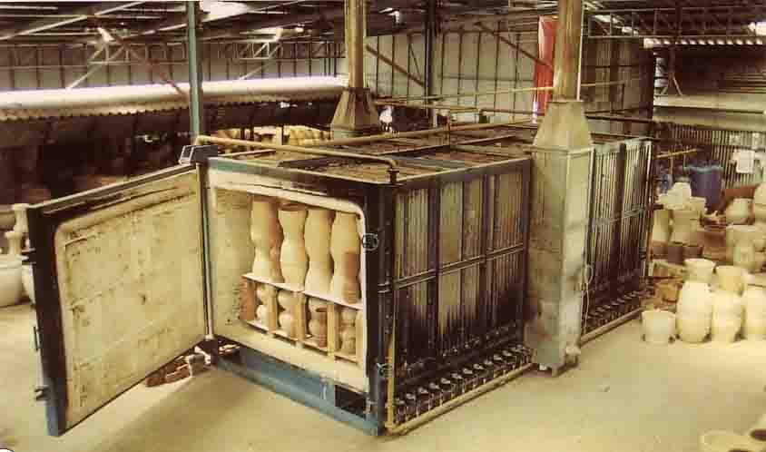 เตาเผาแก๊สแบบรถเข็น (Shuttle Kiln) ในโรงงานเซรามิก ประตูเตาเปิดกว้างมองเห็นชิ้นงานแจกันวางเรียงซ้อนกันบนชั้นทนความร้อนเพื่อเตรียมเผาหรือเพิ่งเผาเสร็จ